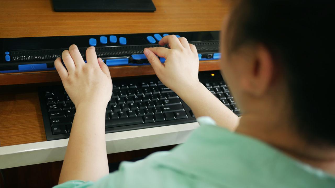 Image of a person with blindess using a braille device to access a website.